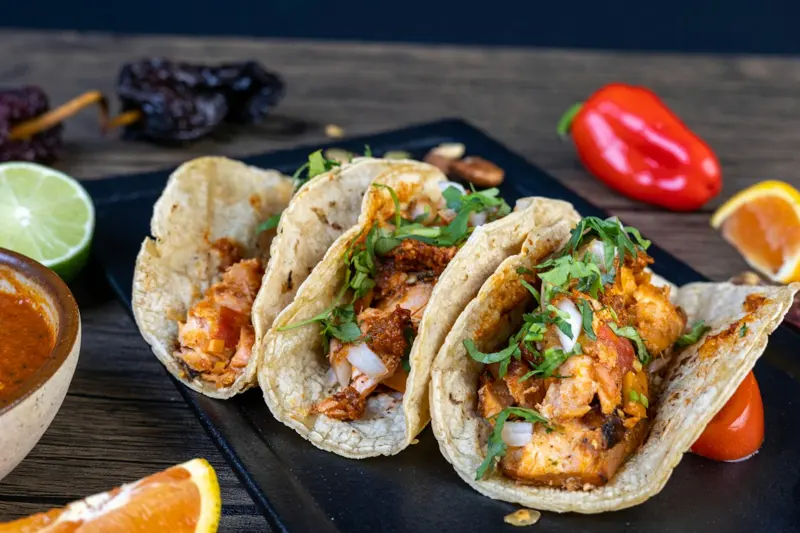 Tres tacos servidos sobre una tabla oscura
